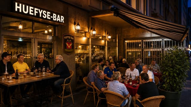 Abendstimmung vor dem Huefyse an der Ahornstrasse im Basler Iselin: der beleuchtete Schriftzug und Gäste an den Tischen unter der Markise