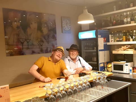 Zwei Stammgäste mit Hüten sitzen am Holztresen in der Quartierbeiz Huefyse im Basler Iselin
